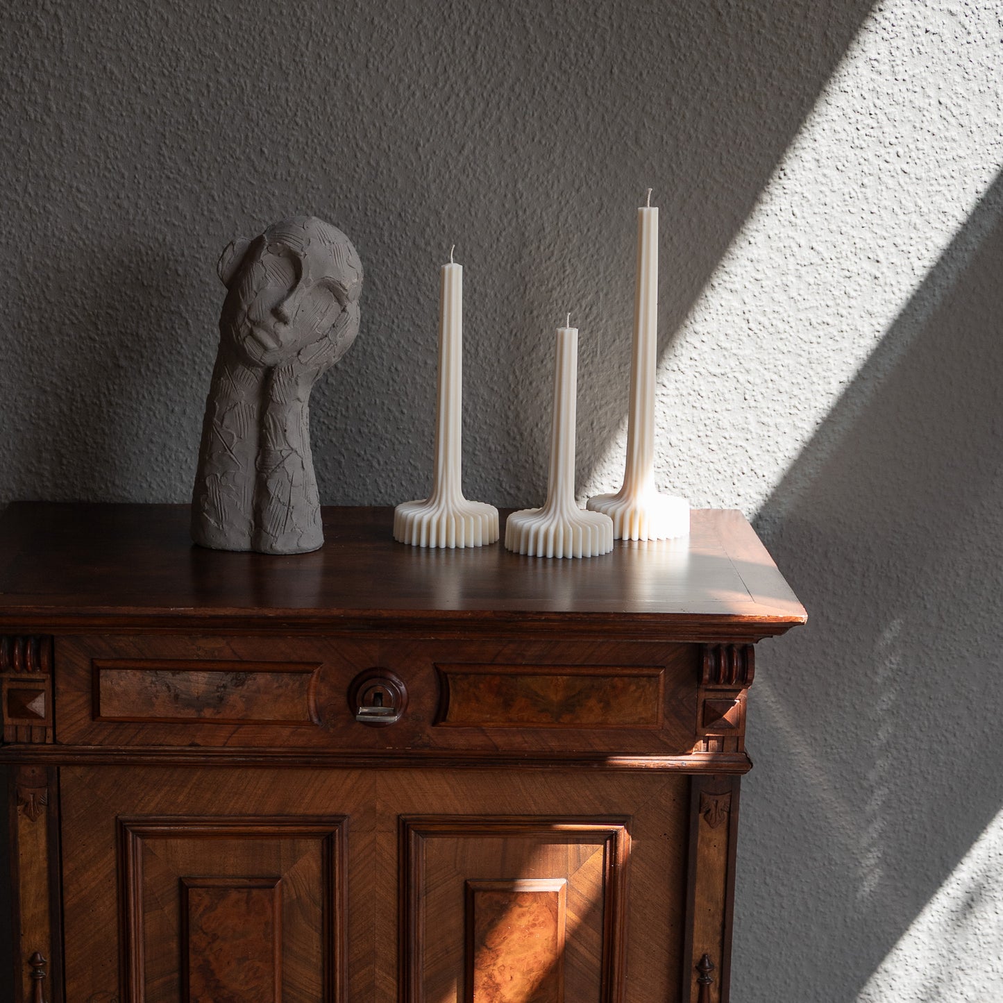 Dreier Kerzen Set Fylda in natürlichem Cremeton – skulpturale Designkerzen, Rapswachs, handgefertigt in Hamburg, 100 % pflanzlich & nachhaltig. Studio Z. Dreier Set mit aufstrebendem Stiel und skulpturalem Plateau. Dekoriert auf barockem Tisch im Schatten-Lichtspiel der Sonne neben nachdenklicher Betonfigur.