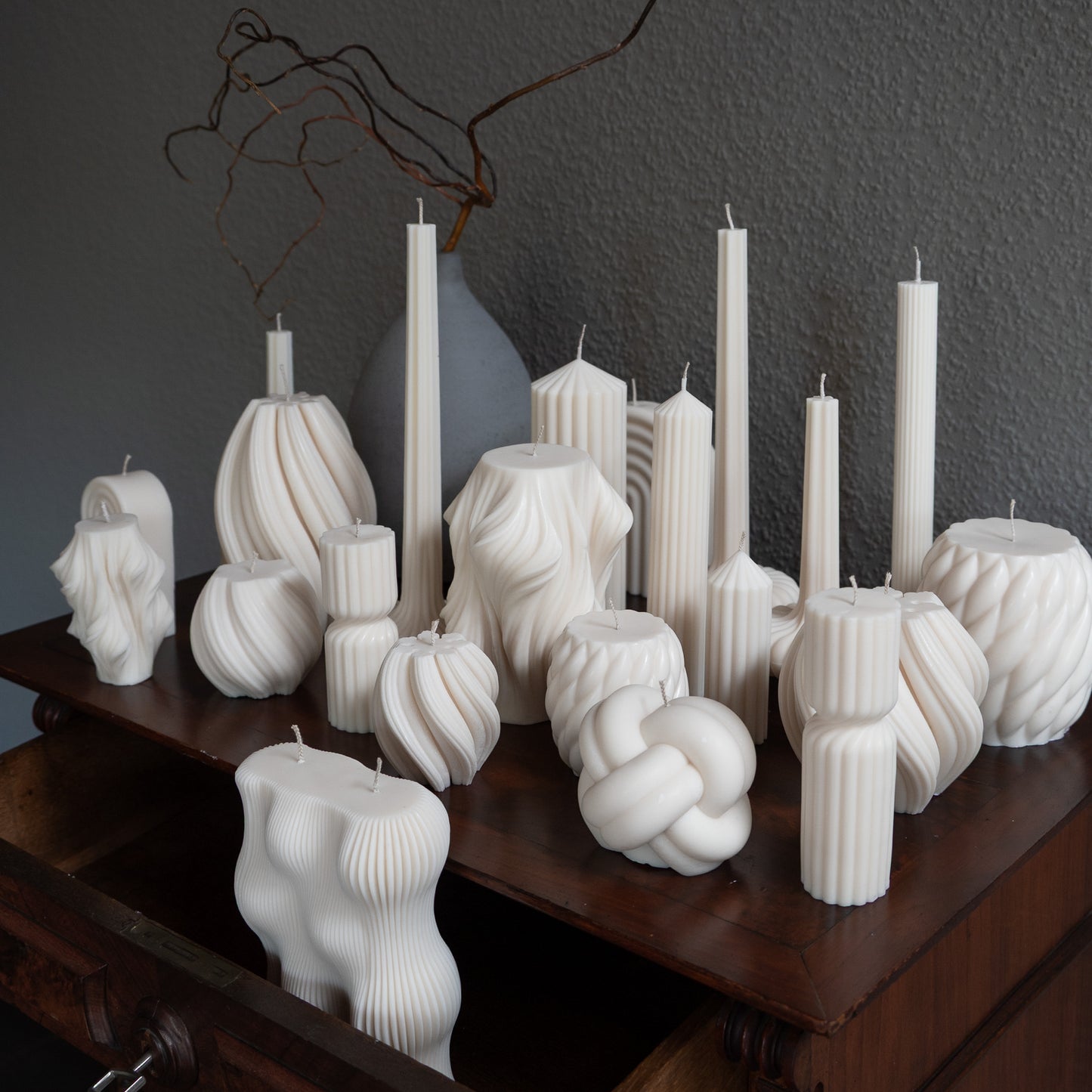 Verschiedene Kerzen Studio Z in natürlichem Cremeton – skulpturale Designkerzen und Stumpenkerzen, Rapswachs, handgefertigt in Hamburg, 100 % pflanzlich & nachhaltig. Dekoriert auf barocker Kommode mit Vase. Væg Bøluna Slør farverig knøt knøv blocka bølge lys