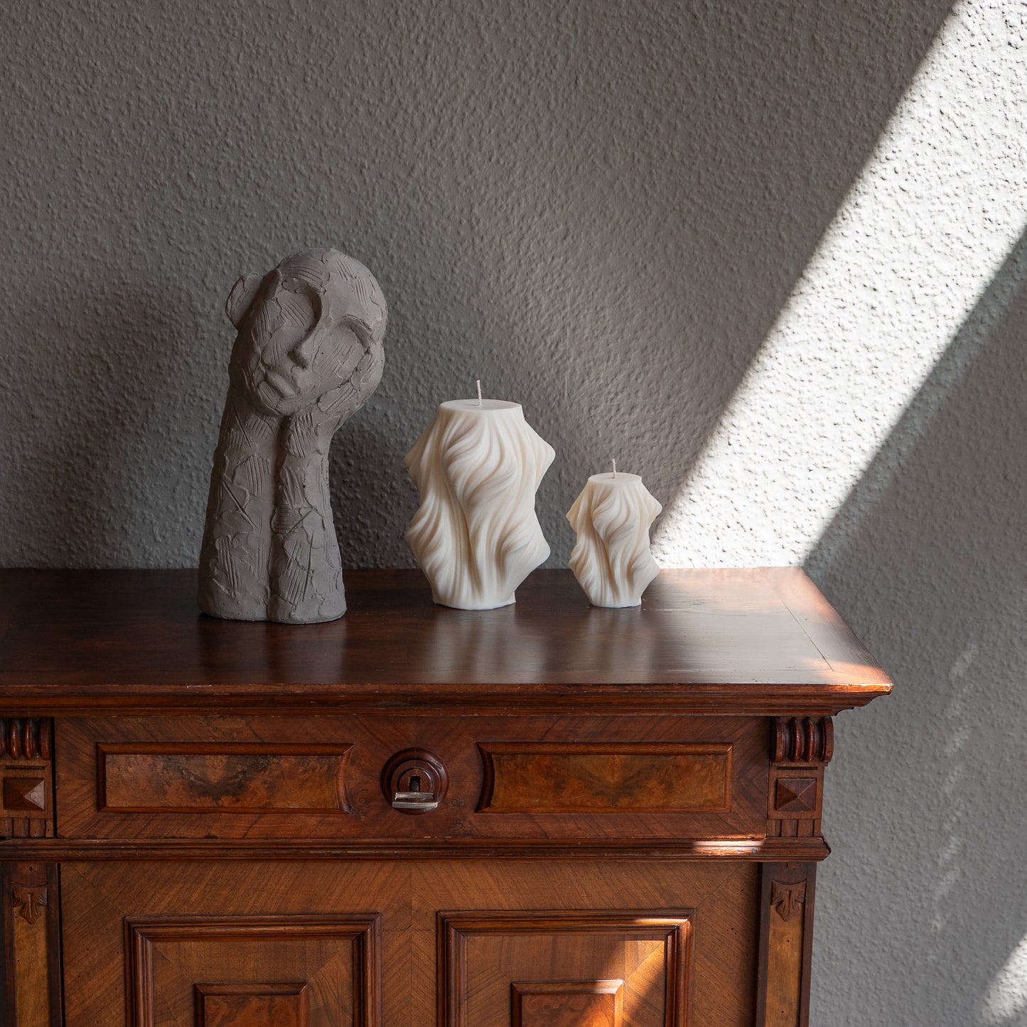 Skulpturale Kerze in Naturfarbe. Handgefertigt in Hamburg – Statement-Dekor im dänischen Design. 100 % natürliche, nachhaltige Materialien. Jedes Stück ein Unikat. Schleier Optik. Dekoriert auf barocker Kommode im Schattenspiel der Sonne neben dekorativem Objekt.
